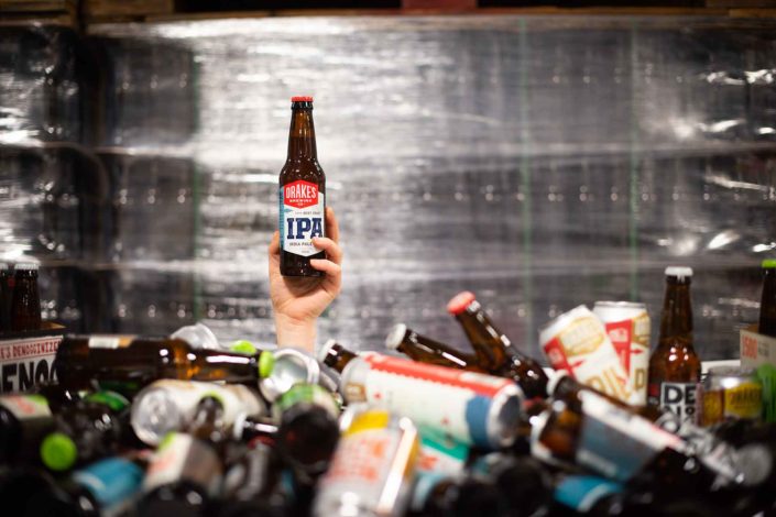 A bottle of IPA being held above a piel of cans and bottles