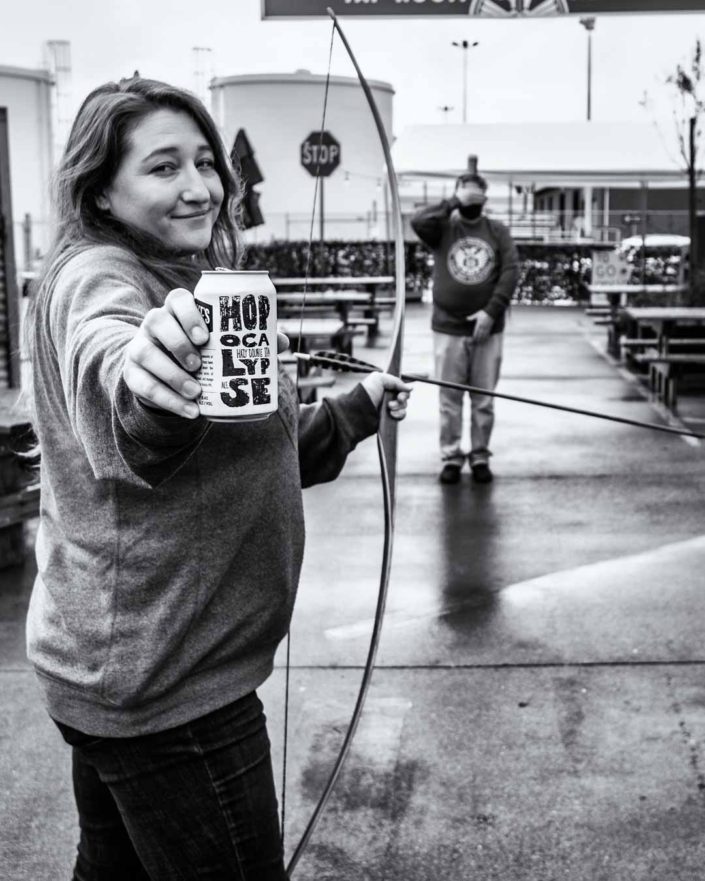 Woman holding a beer can preparing to shoot a bow and arrow